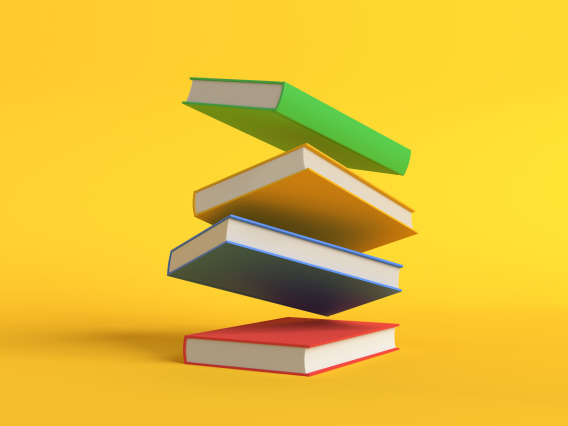 four colored books falling into pile on yellow backdrop